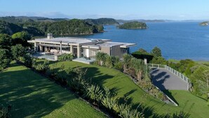 A modern building with a flat roof, surrounded by lush greenery and a body of water. - The Oke Beach House (Rawhiti)
