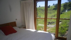 A bedroom with a large bed, a red pillow, and a view of a green landscape through a window.