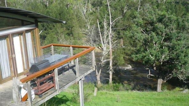 A wooden deck with a glass balustrade overlooking a river and forested area.