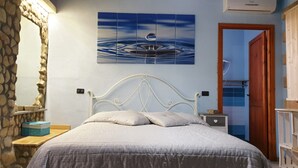 Ein Schlafzimmer mit Steinsturz, einem Bett mit weißem Kopfteil, einem Nachttisch und einem Bild mit Wassermotiv.