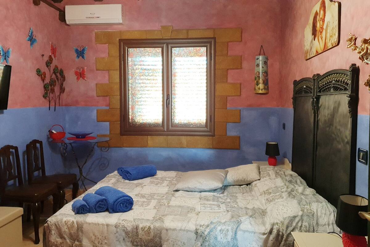Un dormitorio con cama, ventana, televisión, silla, mesa y armario.