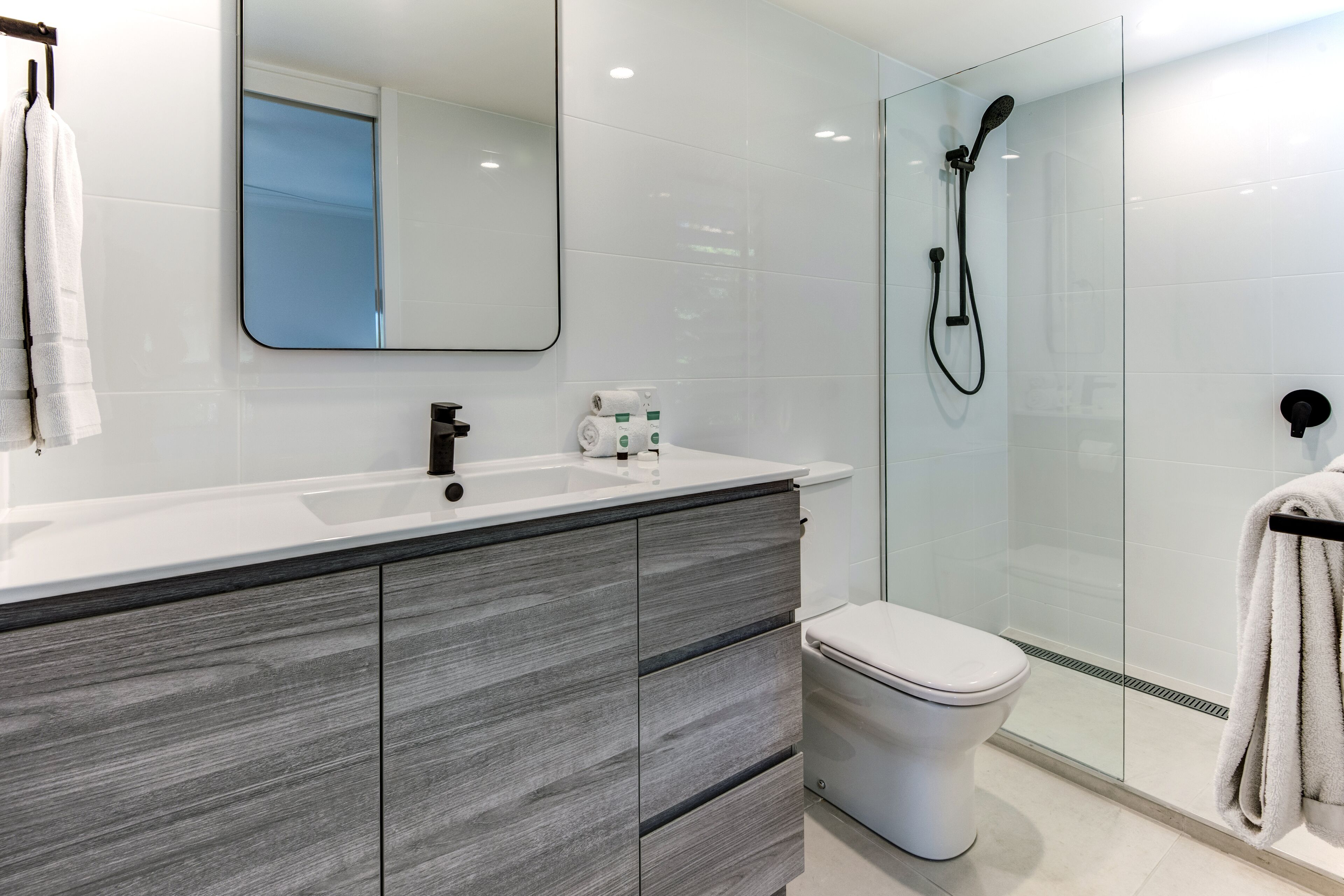 Une salle de bain moderne avec un lavabo blanc, un meuble-lavabo en bois foncé, une cabine de douche en verre et des toilettes.