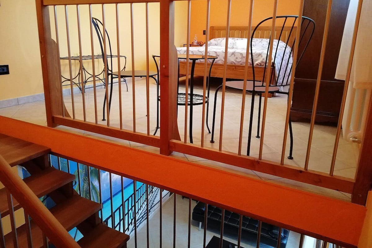 A bedroom with a bed, a chair, and a table. There is a wooden railing in the foreground.
