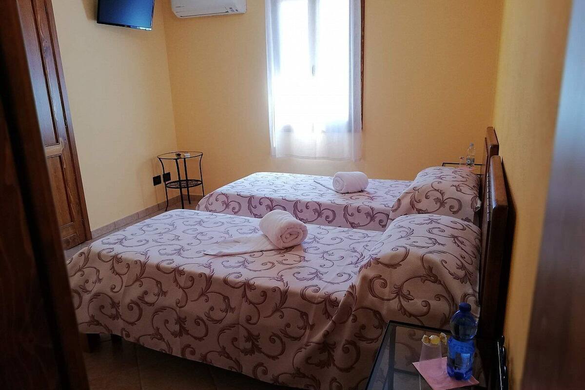 A hotel room with two beds, a small table, a TV, and a window with curtains.