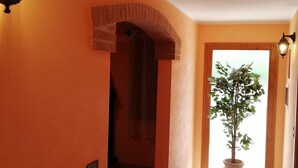 A hallway with orange walls, a tiled floor, a potted plant, and two wall-mounted lights. - Karingo House (Fratta Polesine)