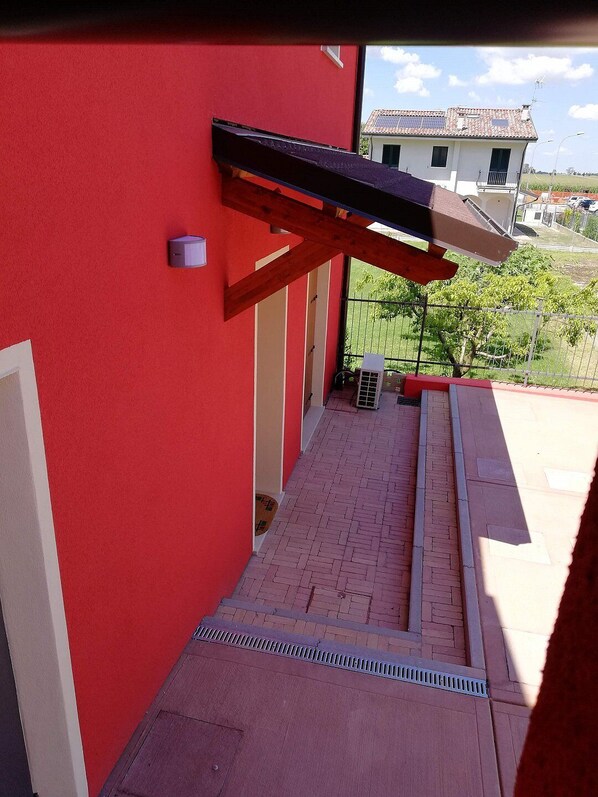 A red building with a covered outdoor area, a brick pathway, and a view of a neighboring house.