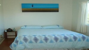 A bedroom with a bed, a painting of a sailboat on the wall, a nightstand, and a window with curtains.