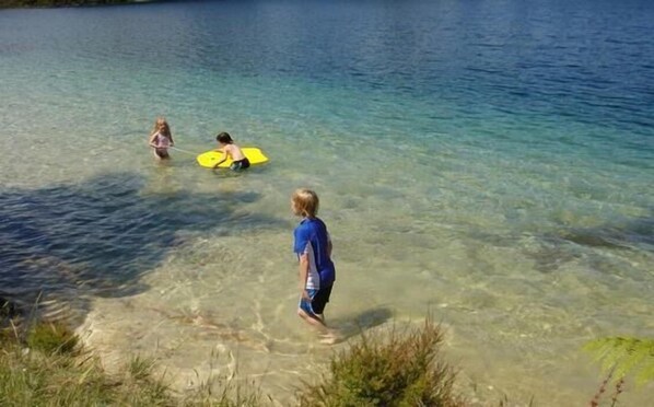 A clear lake with people in the water. - Omamari Beach / Kai iwi Lakes / Kauri Forest (Kai Iwi Lakes)