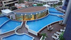 Et tag med swimmingpool opdelt i flere zoner, omgivet af liggestole og en bygning med glasfacade.