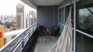 En balkon med et bord og stole, udsigt over bybilledet, samt en gardin.