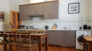 A kitchen with wooden cabinets, a dining table with chairs, a microwave, a kettle, and a washing machine. - The Heritage - located in in the center of Glenelg (Glenelg)