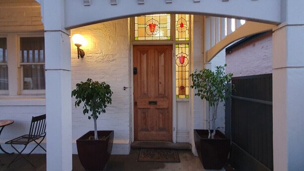 A wooden door with stained glass windows, potted plants, and a bench outside a building. - The Heritage - located in in the center of Glenelg (Glenelg)