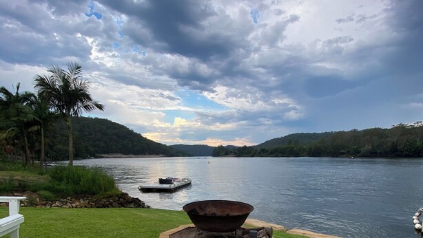 A lakeside setting with a fire pit, a bench, and a glass of pink drink.