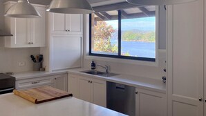 A modern kitchen with white cabinets, a large window with a view, and pendant lights.