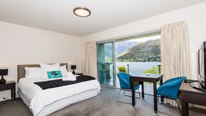 Ett hotellrum med en säng, ett skrivbord och en stol. Det finns ett fönster med utsikt över berg och vatten.