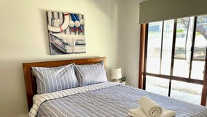 A neatly made bed with striped bedding, a wooden headboard, and a rolled towel on the bed.