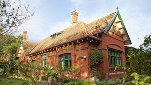 A red brick house with a tiled roof, green shutters, and a garden in front.