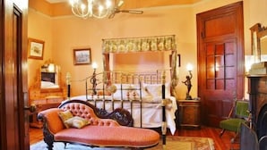 A bedroom with a four-poster bed, a chaise lounge, a wooden dresser, and a fireplace.