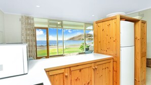 Een moderne keuken met houten kastjes, een wit aanrechtblad en uitzicht op de zee door grote glazen deuren.