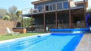 Une maison à deux étages dotée d’une piscine, d’un jacuzzi et d’une terrasse avec des chaises.