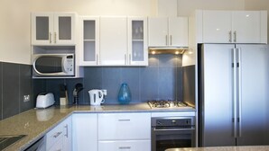 Une cuisine moderne avec des armoires blanches, un four à micro-ondes encastré, une cuisinière à gaz et un réfrigérateur en acier inoxydable.
