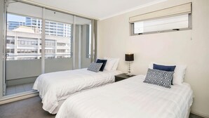 Hotellihuone, jossa on kaksi sänkyä, suuri ikkuna, josta on näkymä rakennuksiin, kattovalaisin ja seinälle kiinnitetty peili.