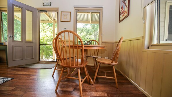 A dining area with a wooden table and chairs, a door leading outside, and a window with a view of trees.