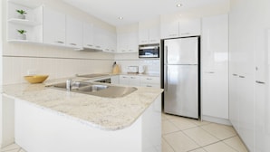 A modern kitchen with white cabinetry, a stainless steel refrigerator, a microwave, and a granite countertop. - 3 Bedroom Penthouse Apartment with a Private Rooftop Spa (Sunshine Coast)