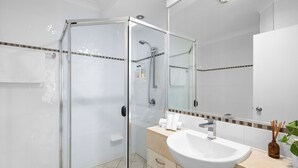 A modern bathroom with a glass-enclosed shower, a white sink, and a mirror with a decorative tile border. - 3 Bedroom Penthouse Apartment with a Private Rooftop Spa (Sunshine Coast)