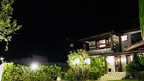 A swimming pool with a tiled edge, surrounded by a paved area. There is a building with multiple windows and a balcony in the background. - Cozy and charming house with pool and gardens in a beachfront condominium! (Camaçari)