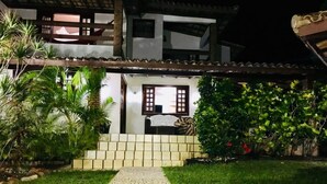A pathway leading to a building with a tiled entrance and a small porch area. - Cozy and charming house with pool and gardens in a beachfront condominium! (Camaçari)