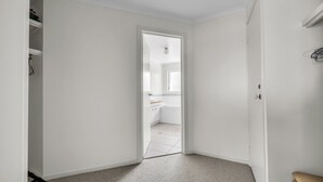Un couloir menant à une salle de bain dotée d’une fenêtre, de murs blancs et d’un sol carrelé.