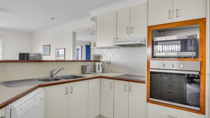 Une cuisine compacte avec des meubles blancs, un four à micro-ondes encastré, un four traditionnel et un lave-vaisselle.