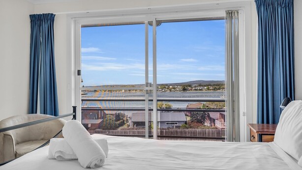 Une chambre d’hôtel dotée d’une grande porte-fenêtre coulissante donnant sur un balcon avec vue sur un pont et des immeubles.