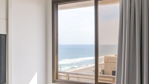 A hotel room with a large window offering a view of the beach and ocean.