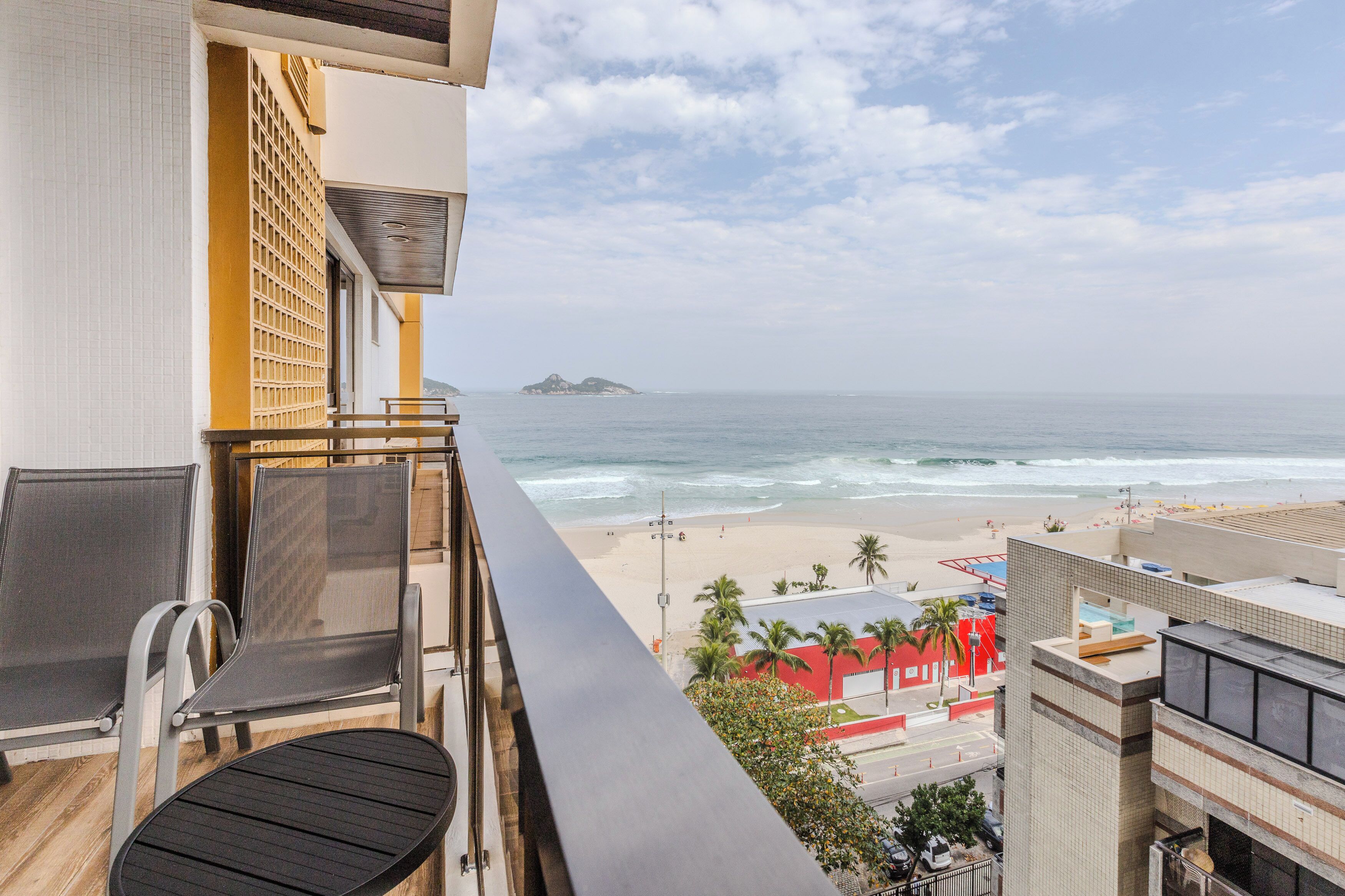 A balcony with a view of the beach and ocean, a chair, and a table.