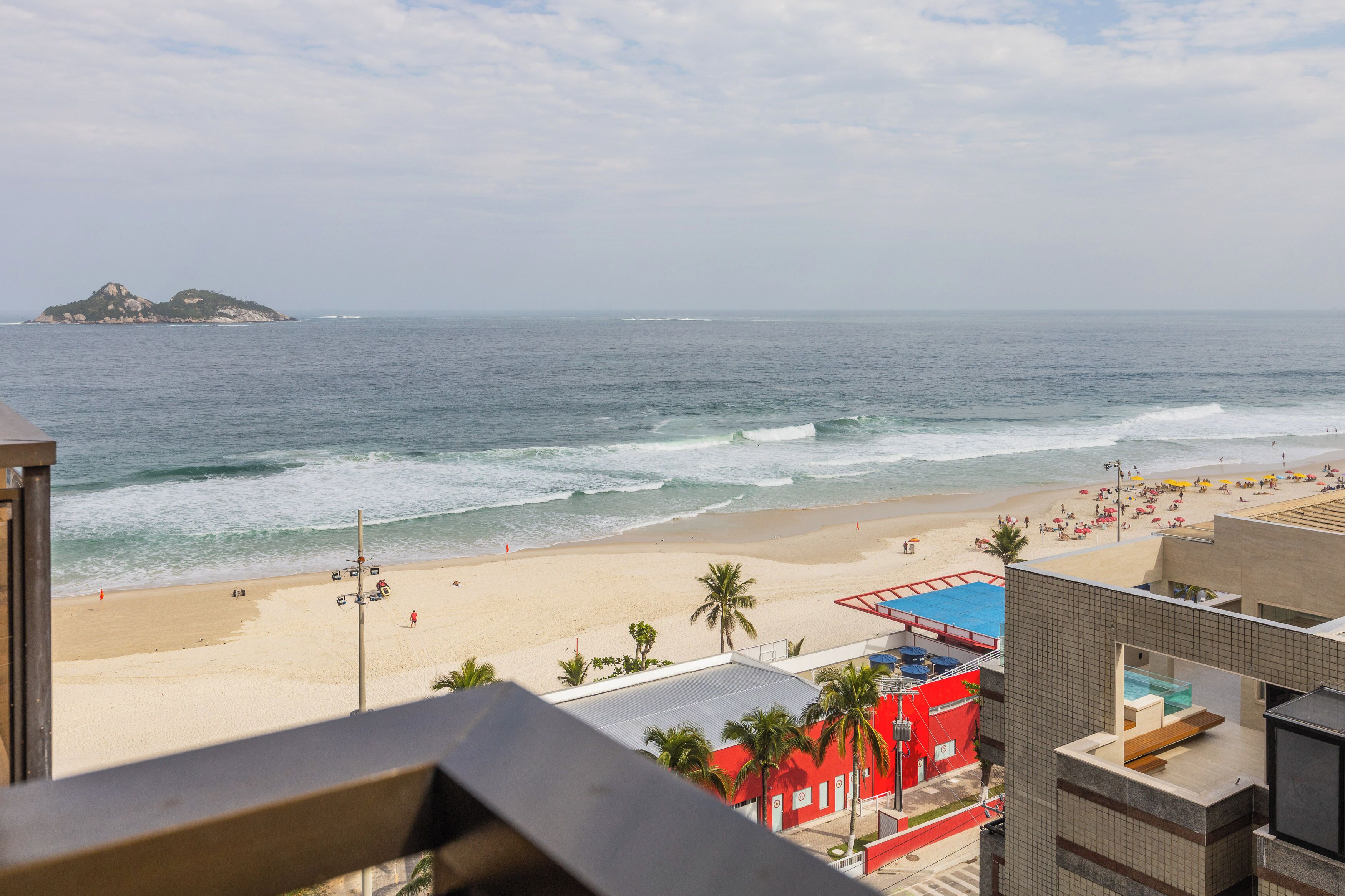 Vista de la playa con un edificio al frente, arena y el océano.