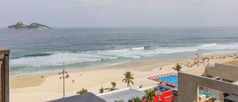 Vista de la playa con un edificio al frente, arena y el océano.