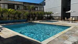 A rectangular pool with clear blue water, surrounded by tiled flooring and palm trees.
