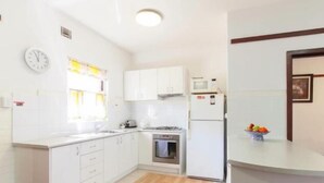 A compact kitchen with white cabinets, a microwave, an oven, and a clock on the wall. - B4 UWA, Swan River, Hospitals, CBD (Crawley)