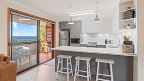 Una cocina moderna con una isla grande, taburetes de bar y vistas al océano a través de una puerta corredera.