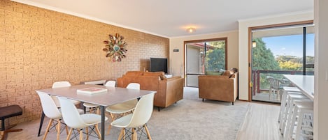A modern living space with a brick wall, a dining area with a table and chairs, a sofa, and a balcony with a view.