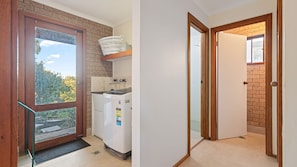 Cozinha compacta com geladeira, máquina de lavar e janela com vista para árvores.