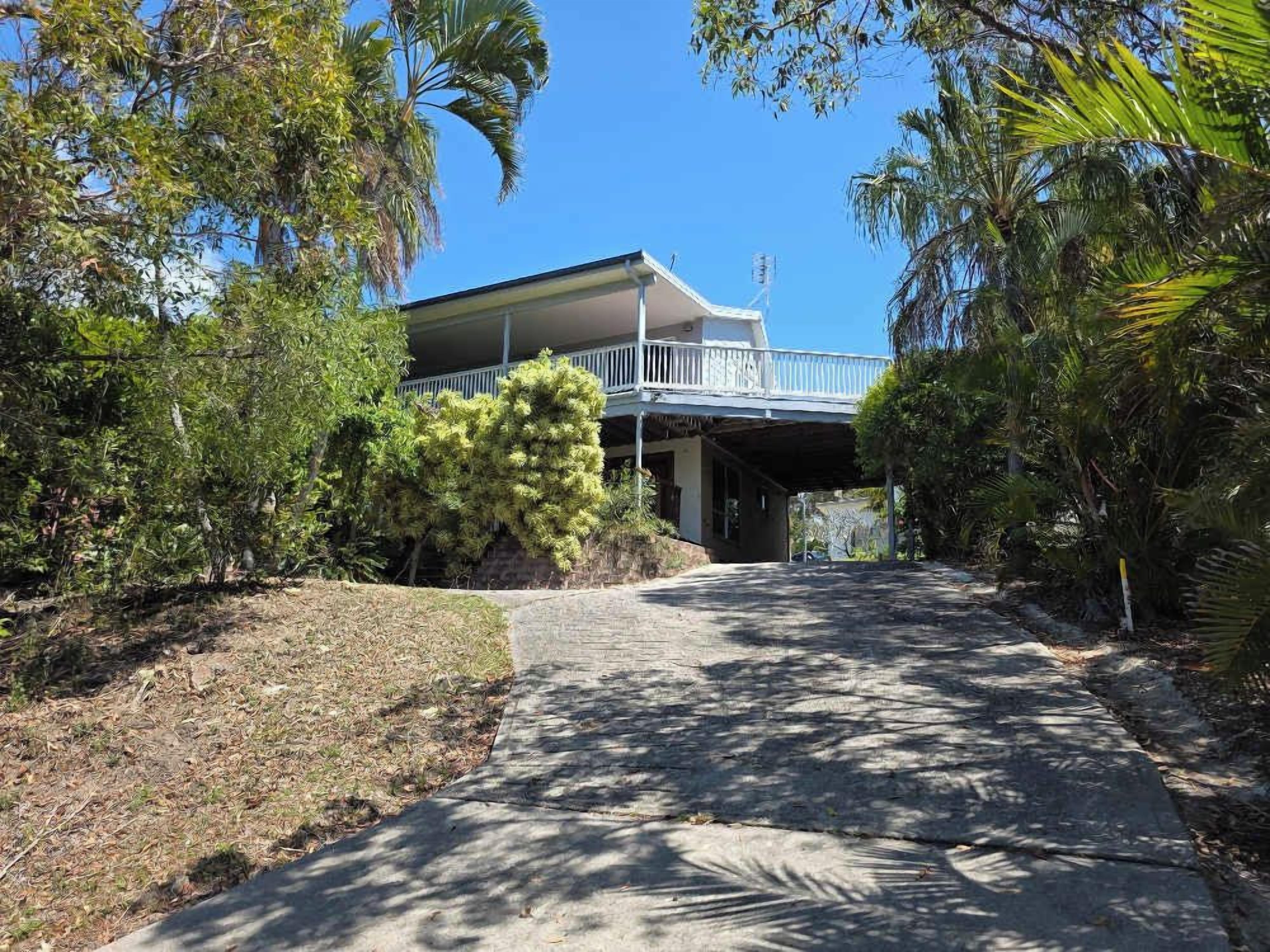 Une maison à deux étages dotée d’un balcon, entourée d’une végétation tropicale luxuriante.