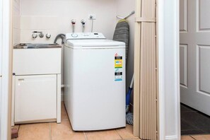 Un espace réduit dédié à la buanderie, comprenant un lave-linge, un évier et un balai.