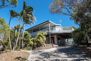 A two-story house with a balcony, surrounded by trees and a clear sky. - Arbour Rest Expansive Ocean Views (Agnes Water)