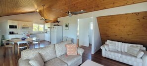 A spacious living area with a sofa, a dining table with chairs, and a kitchen area with cabinets and a refrigerator. - Arbour Rest Expansive Ocean Views (Agnes Water)