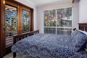 Une chambre à coucher avec un lit, une fenêtre avec des stores et une porte munie d’une grille en métal.