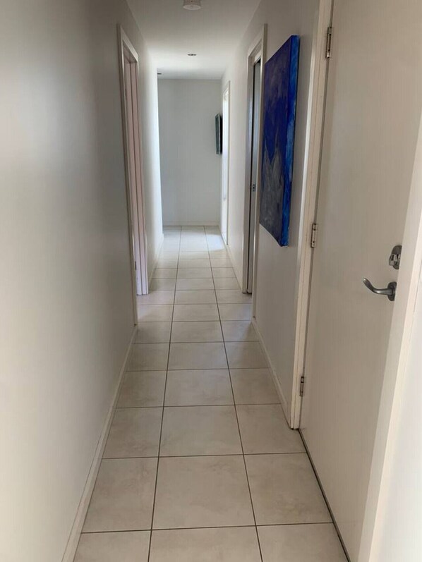A narrow, tiled hallway with white walls and doors on either side. - Casey’s Beach Retreat (Batehaven)