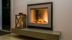 A fireplace with a stone mantle, a wooden lantern, and a view of greenery outside.